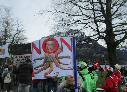 Demo in Brunnen auf der Seewiese:
                  Das Plakat mit Tedros als Krake / Tintenfisch mit Bill
                  Gates im Hintergrund